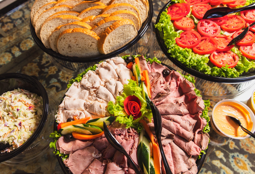 A photo of deli meats, bread and tomatoes. With Coleslaw